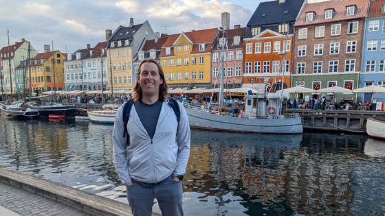 Brian standing by a the Hyhavn Canal in Copenhagen Denmark with colorful waterfront buildings and boats