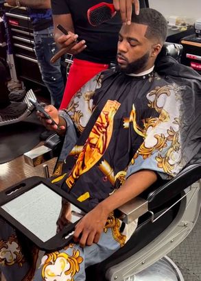 A man is sitting in a barber chair getting his hair cut.