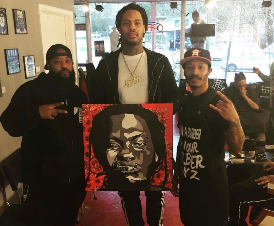 Three men are standing in a barber shop holding a painting of a man 's face