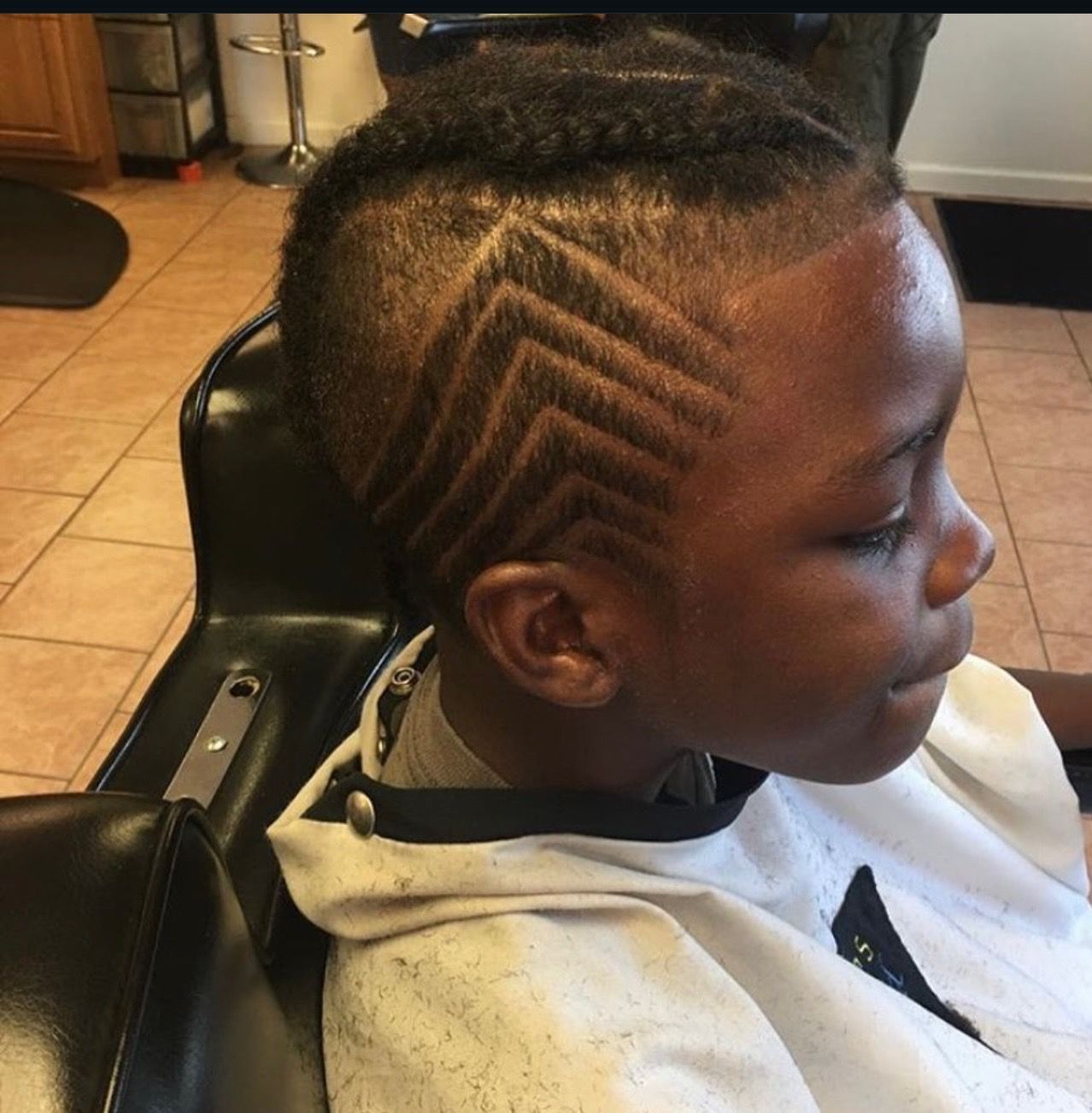 A young boy is sitting in a chair with a braided design in his hair