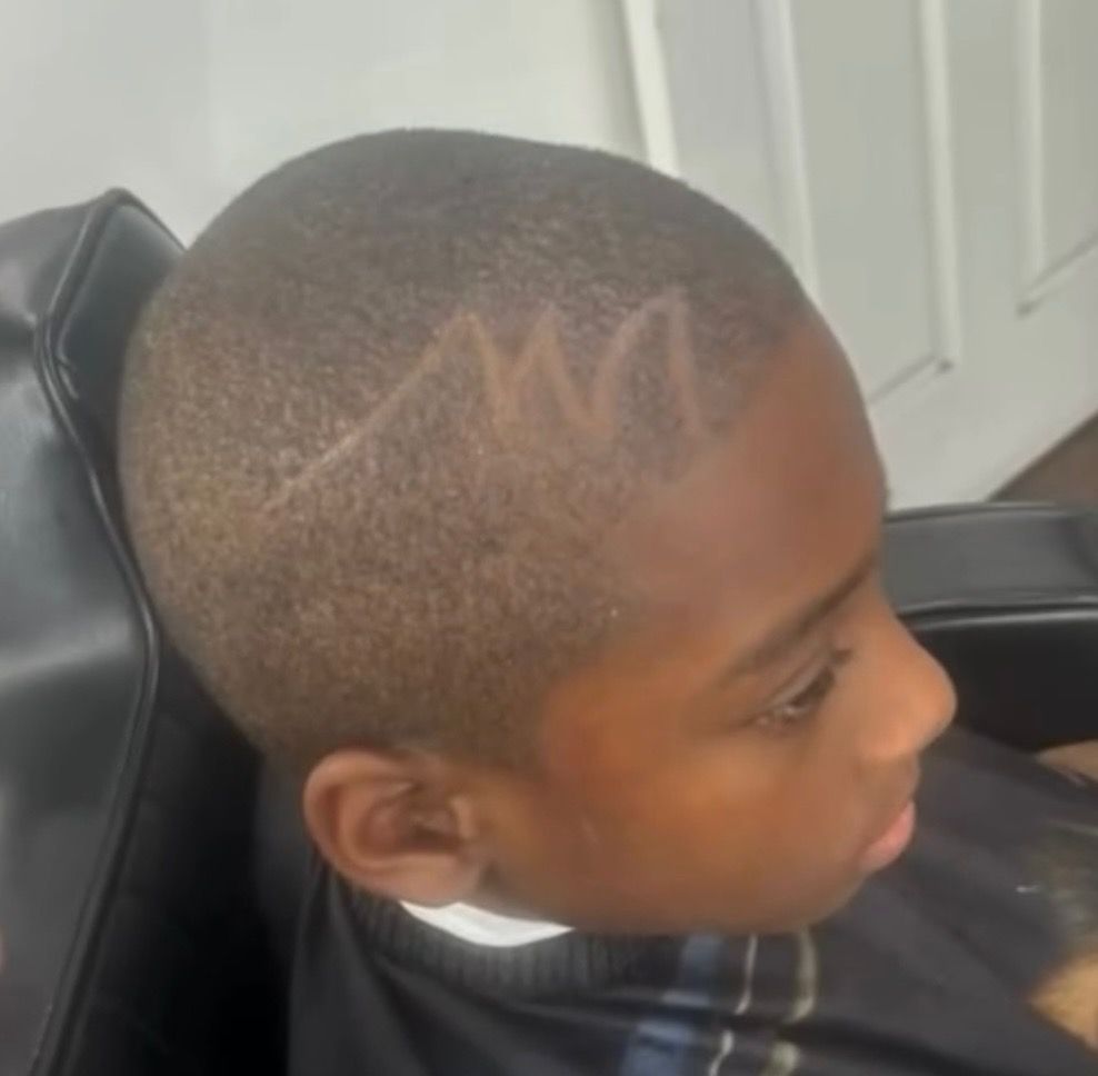 A young boy is sitting in a chair with the letter m carved into his hair