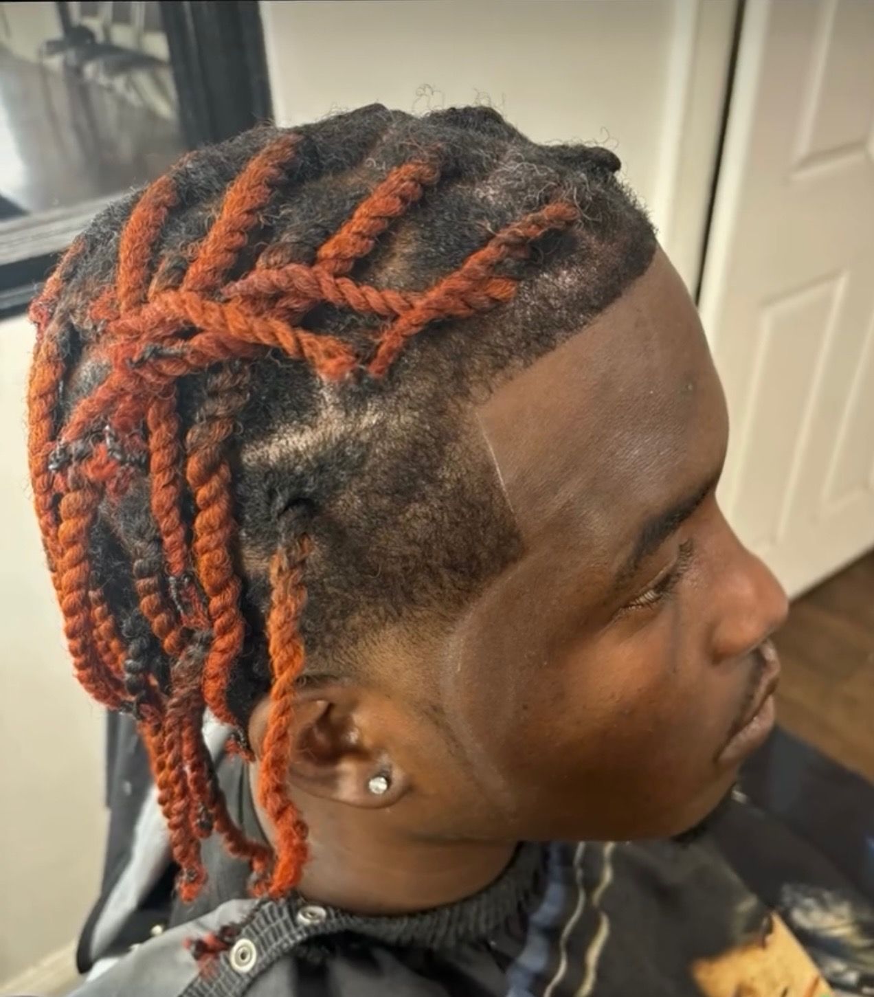 A man with red dreadlocks is wearing a black cape