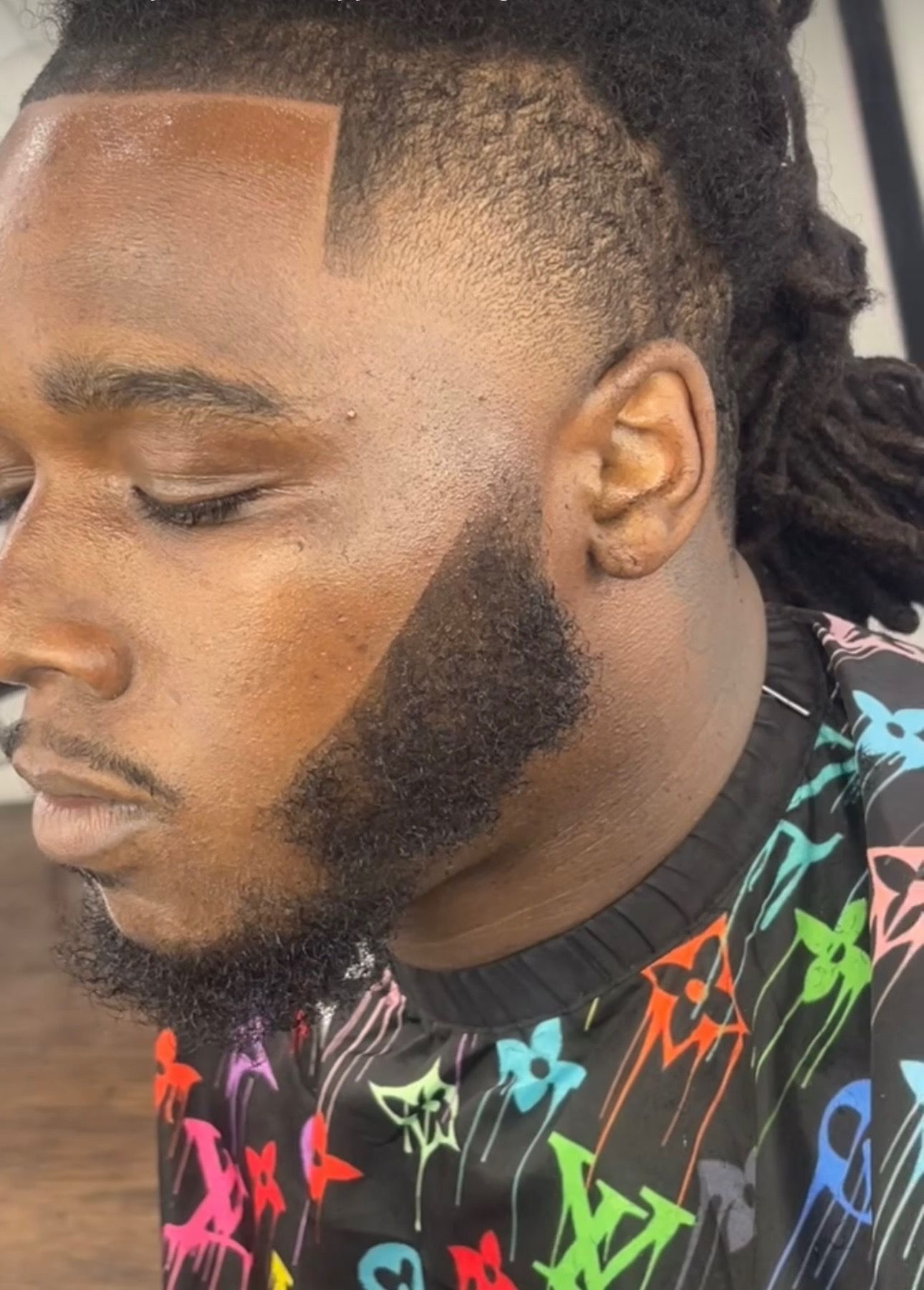 A man with dreadlocks and a beard is wearing a louis vuitton shirt.