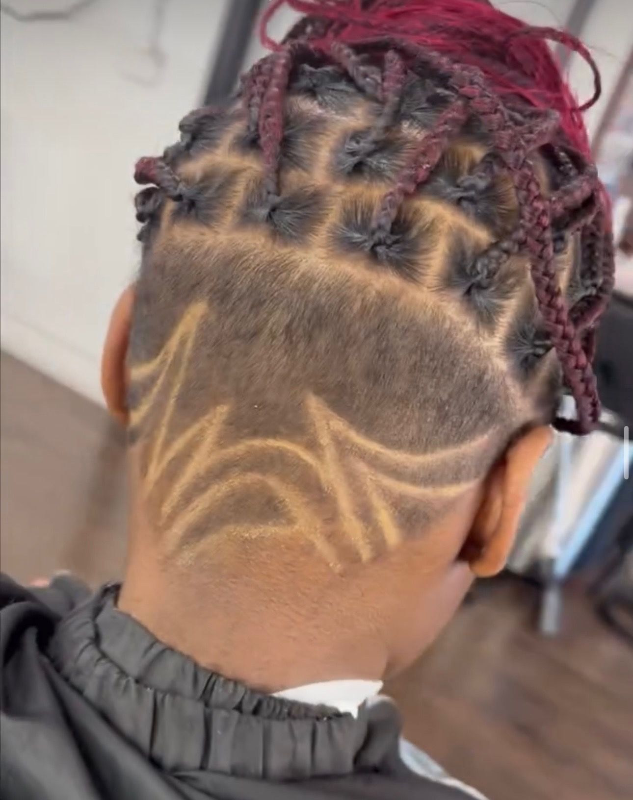 A person with braids and a shaved design on the back of their head.