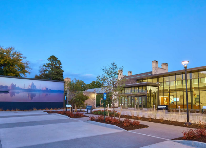 Exterior view of a modern building with a parking lot and a mural of a landscape on the left.