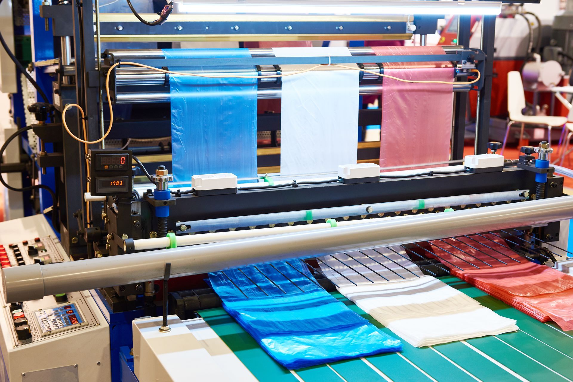 Plastic bag manufacturing machine with blue, white, and red rolls of plastic material.
