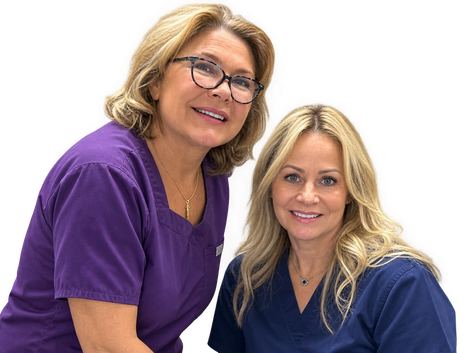 Two smiling women in purple and navy scrubs posing together against a white background