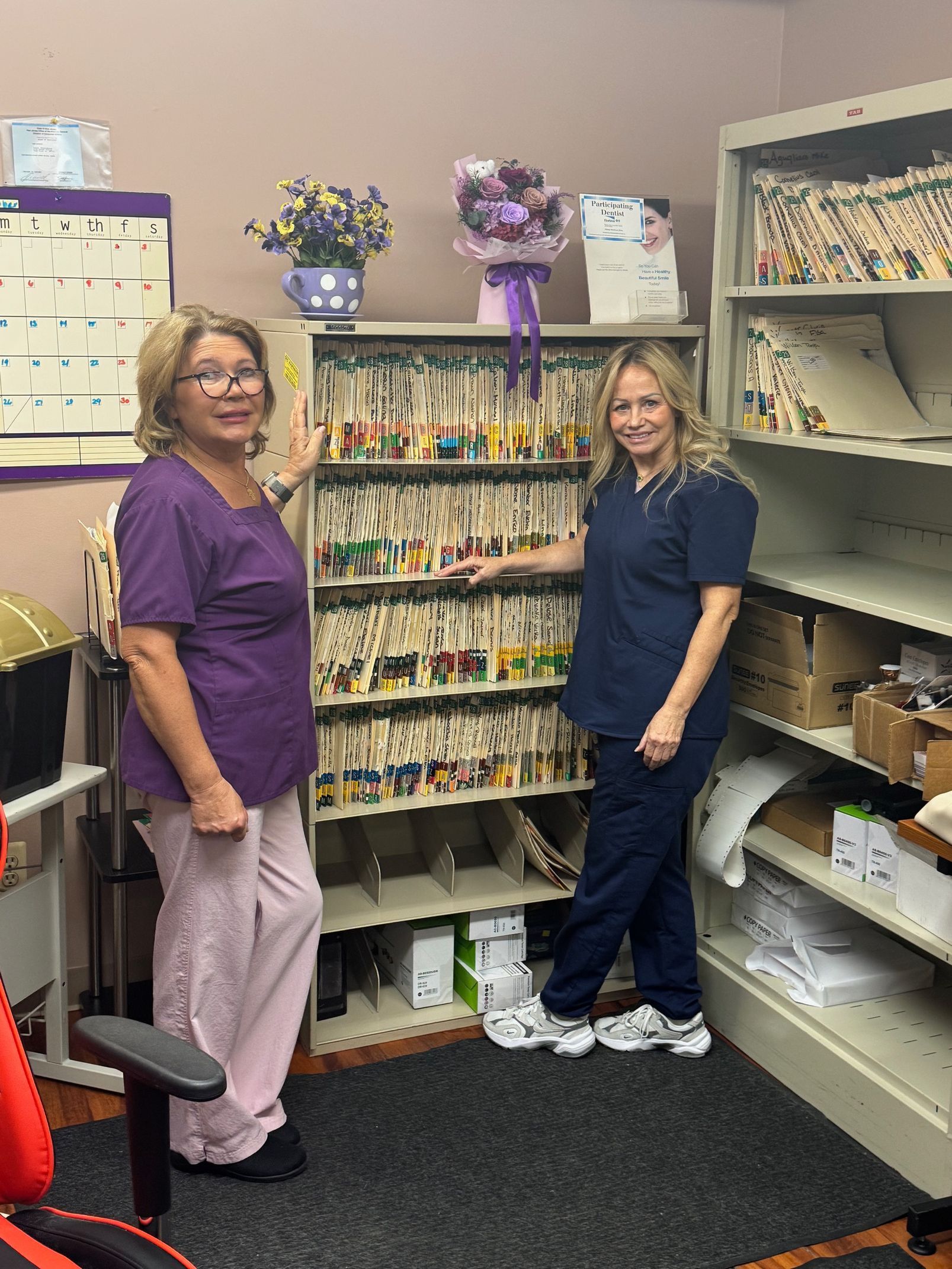 Two women standing in a craft room beside shelves of ribbon, supplies, and decorated boxes