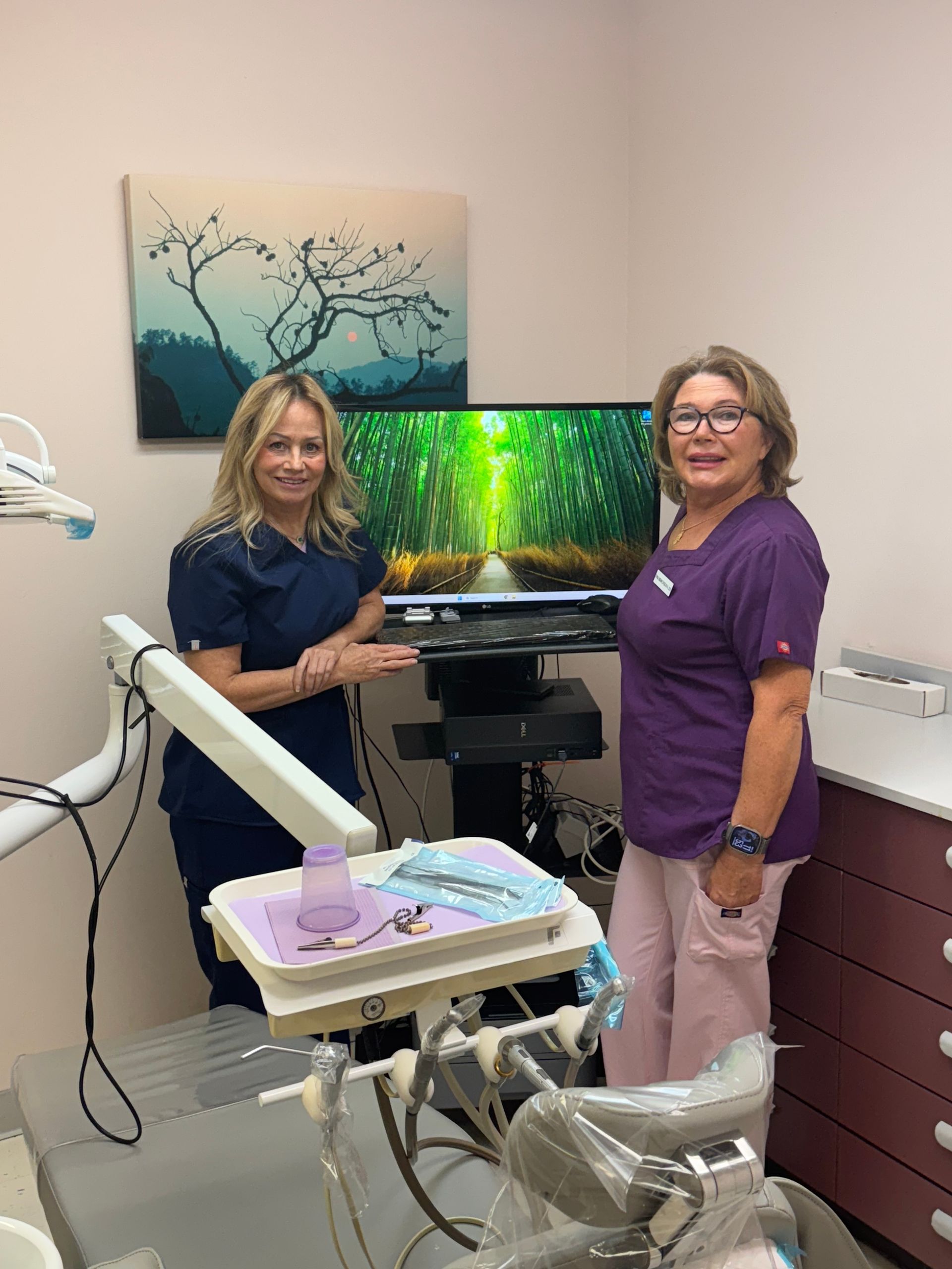 Dental office with two clinicians beside an exam chair and monitor displaying nature scene