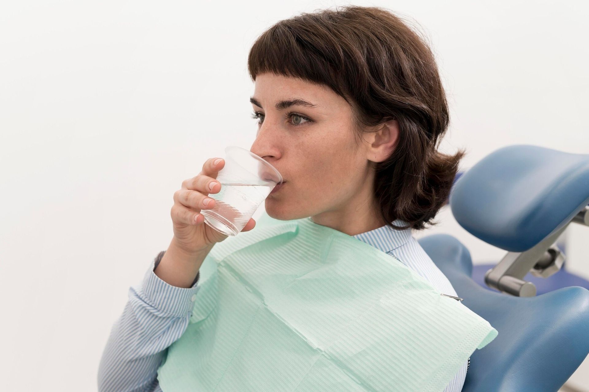 Person drinking water in a dental chair with a green bib, after a treatment.