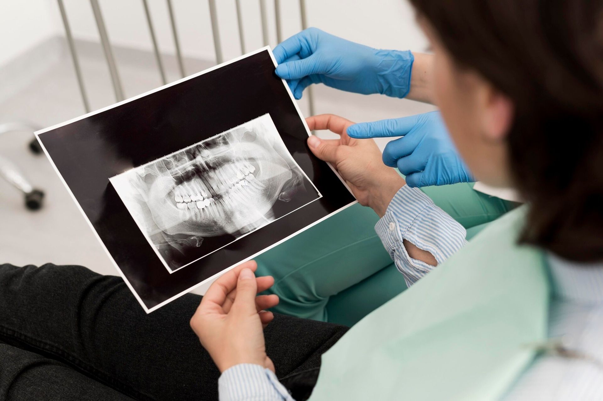 Dentist showing a dental X-ray to a patient in a clinic, with gloved hands holding the film.