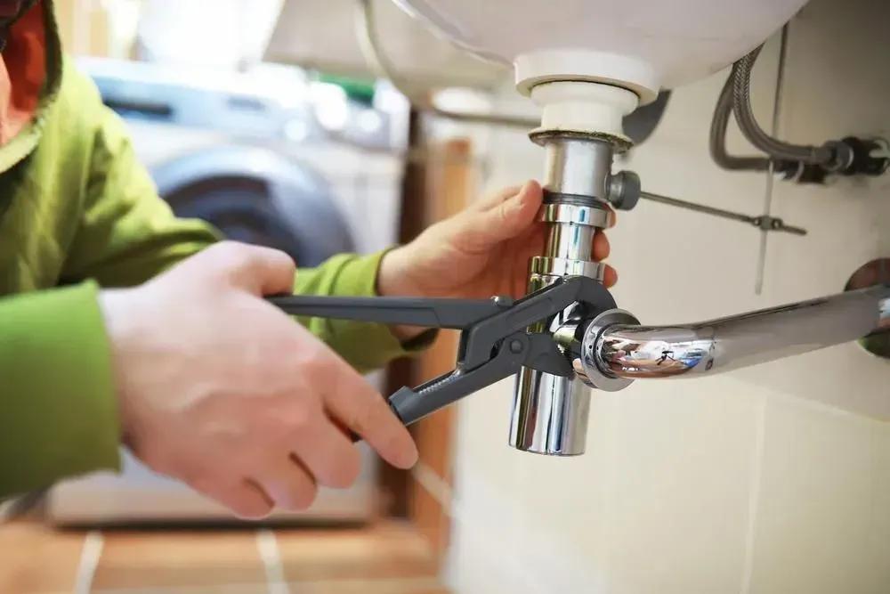 Hands using a wrench to tighten a chrome pipe under a sink