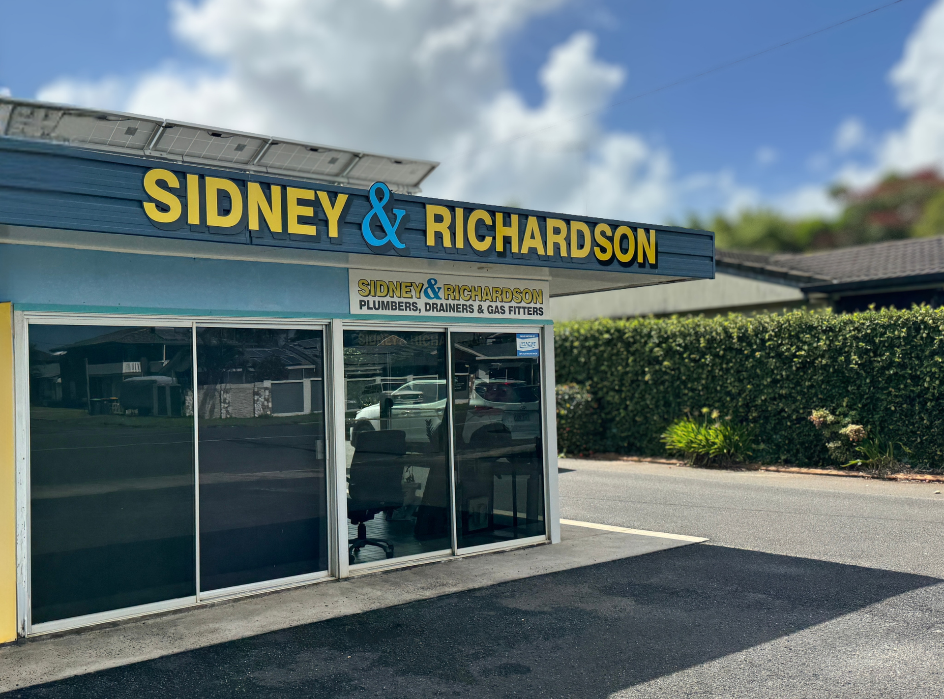 Sidney & Richardson storefront with blue sign, red “HEATING” banner, and parking lot under a bright sky