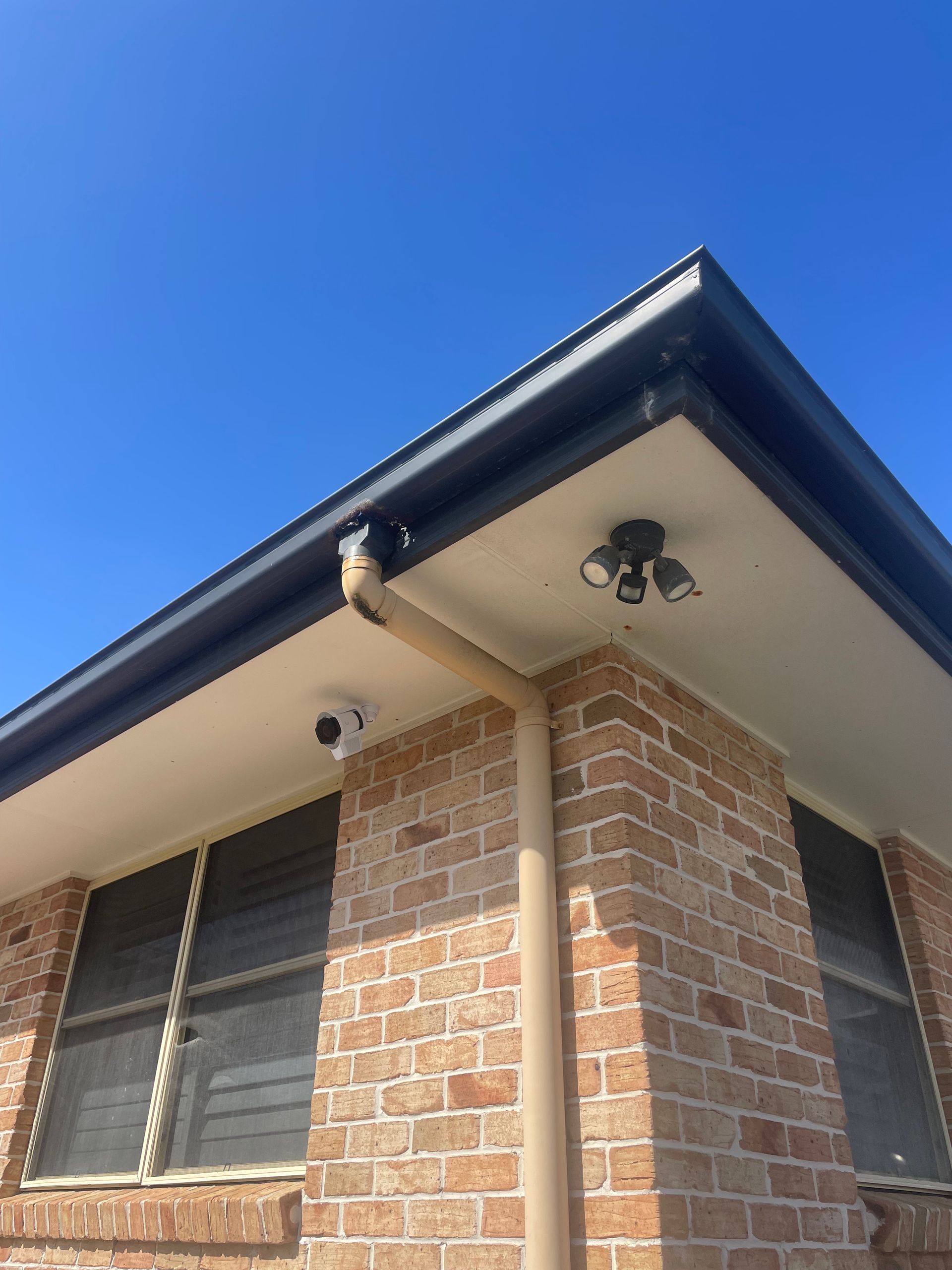 Corner of a brick house under a blue sky, with windows, guttering, and an exterior light fixture