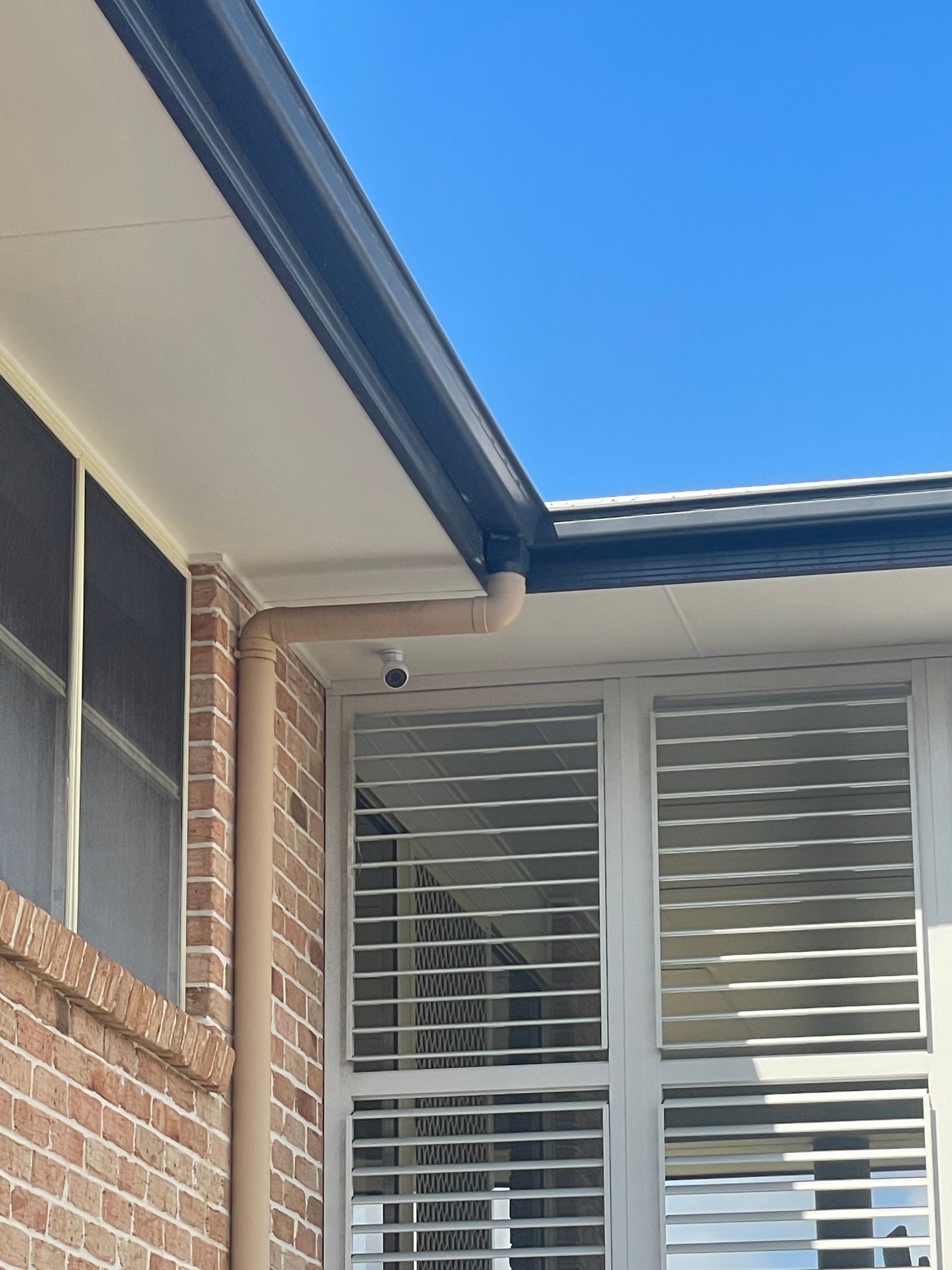 Brick house exterior with white shutters and a tiled roof under a blue sky