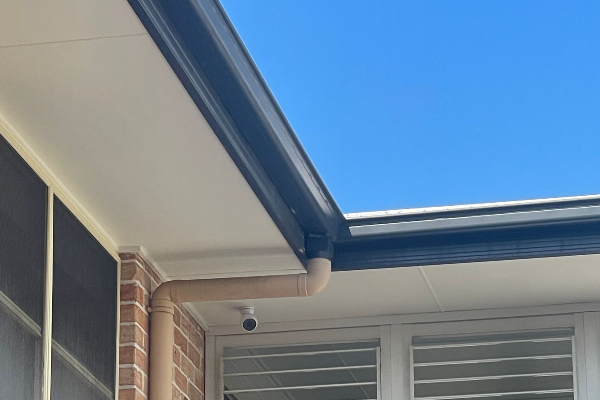 House eaves and brick exterior with a blue sky overhead and a security camera mounted near the roofline