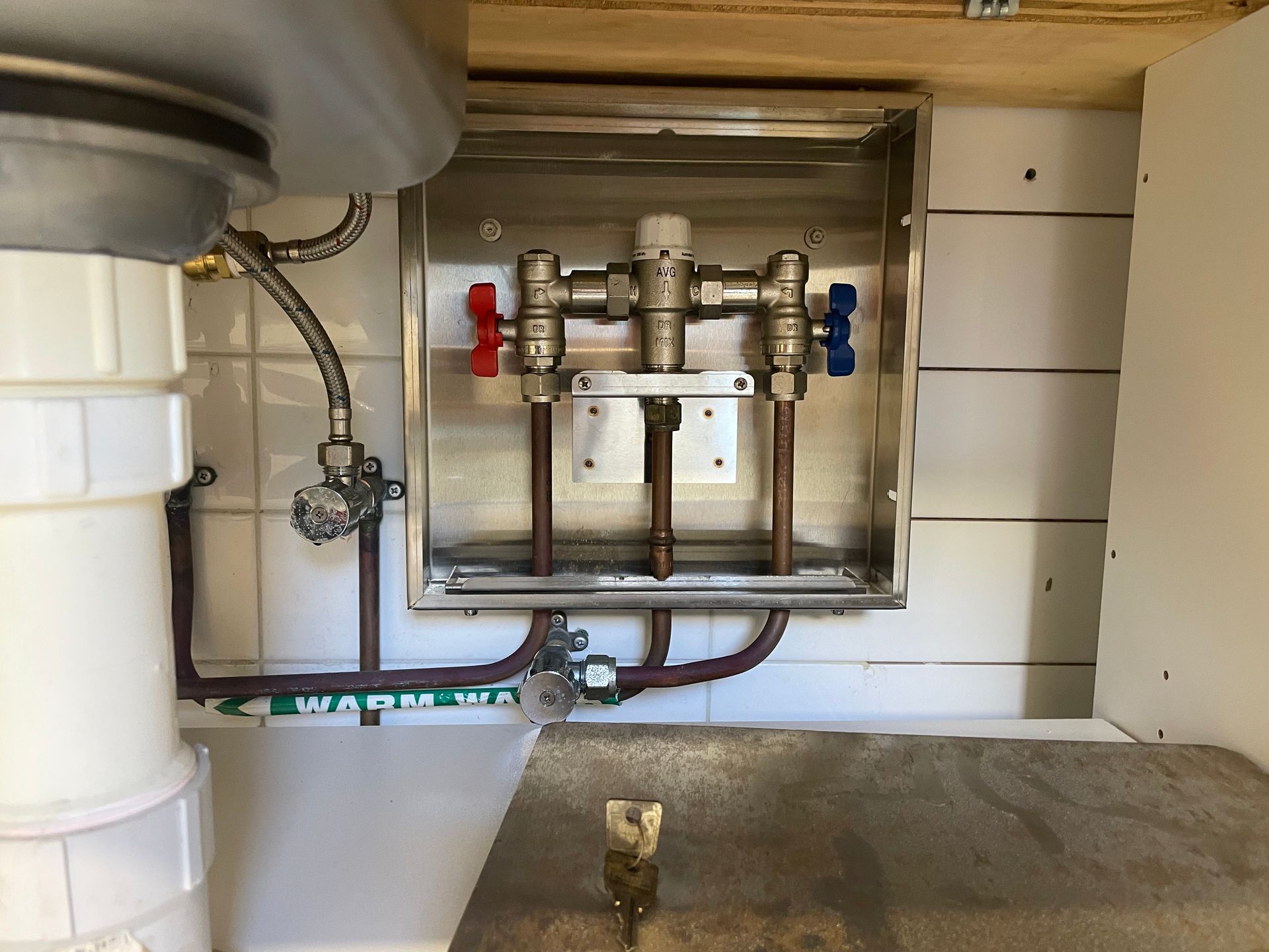 Under-sink plumbing with exposed valves and pipes on a tiled wall above a countertop
