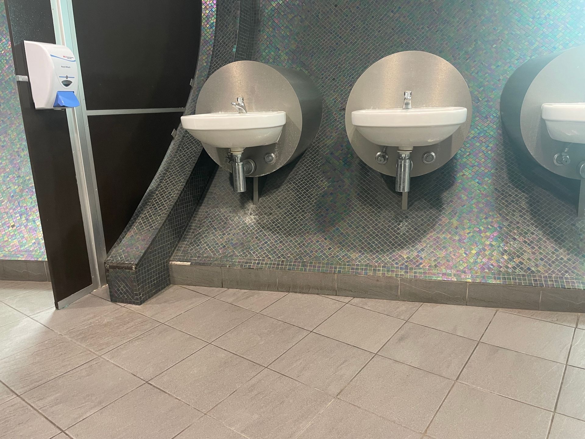 Public restroom with two wall-mounted sinks, speckled dark walls, and tiled floor