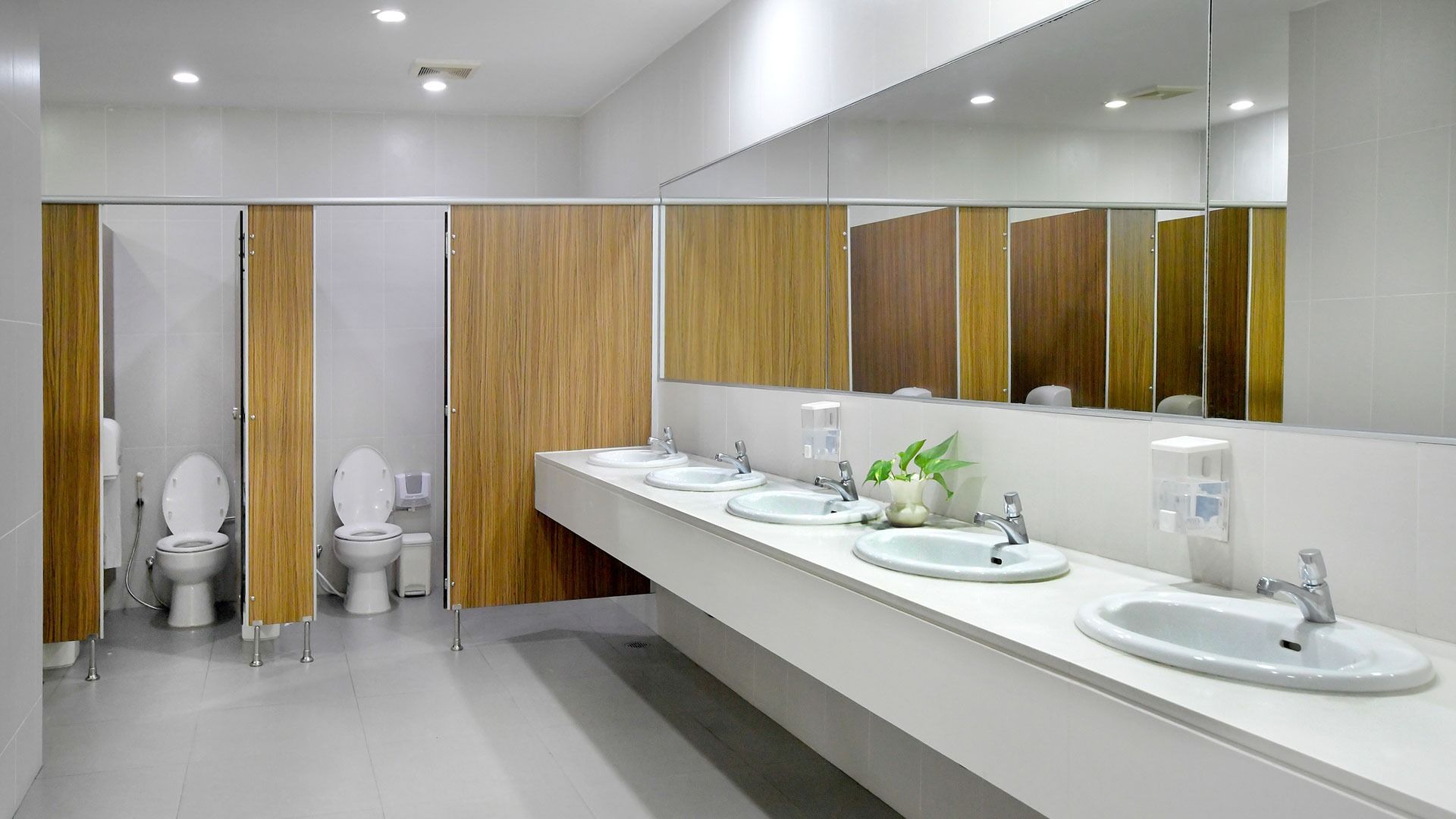 Modern public restroom with wood stalls, white sinks, large mirrors, and bright lighting