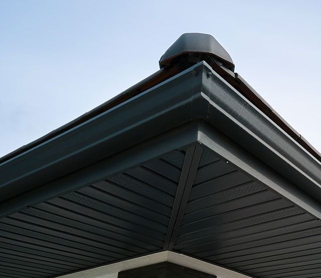 Close-up of a house roof corner with gray soffit and dark shingles against the sky