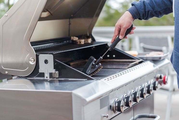 Person grilling food on a stainless steel barbecue with the lid open and a spatula in hand