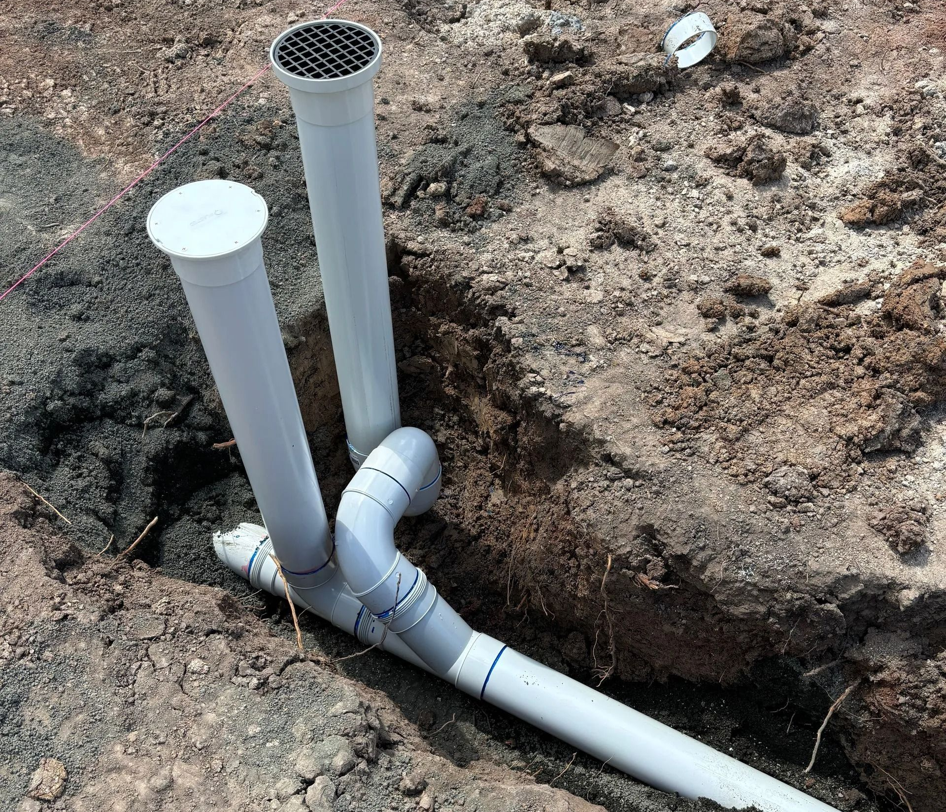 White PVC pipes and fittings installed in a dirt trench at a construction site