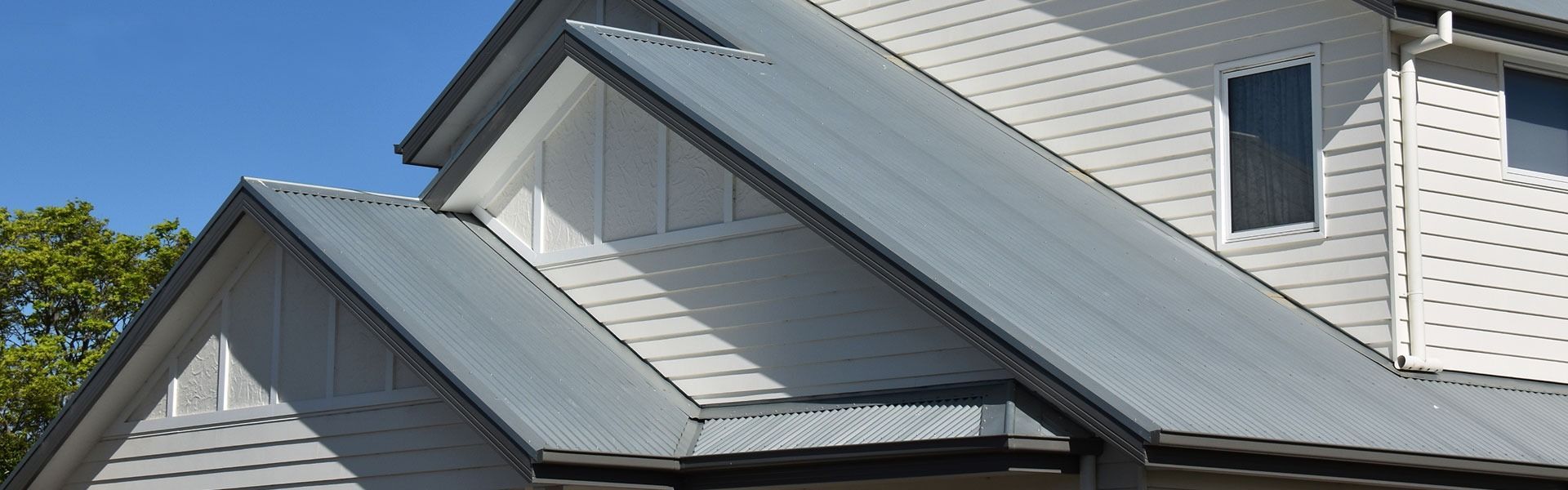 Gray metal roofs on a white house with dormers under a blue sky.