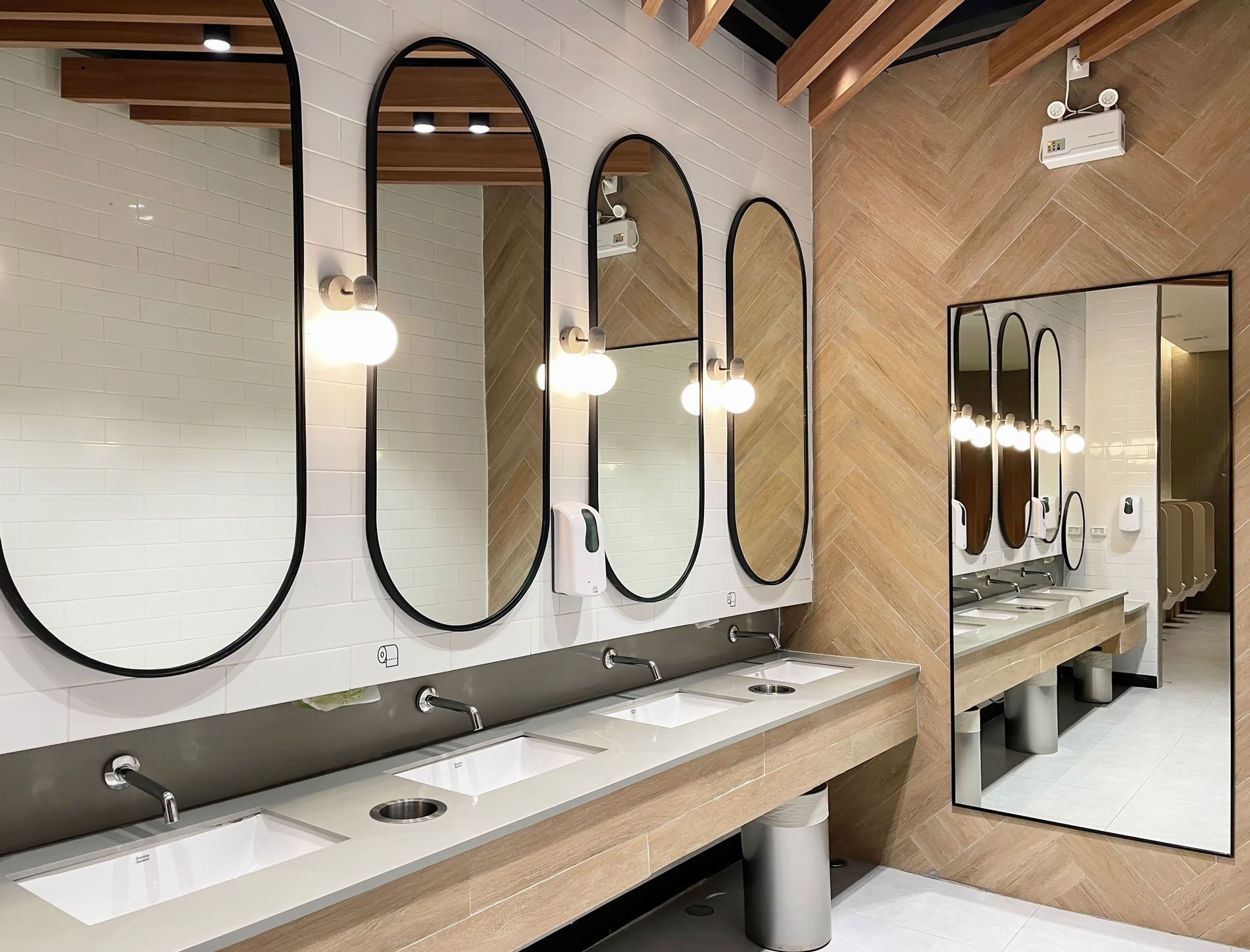 Modern restroom with long sinks, oval mirrors, pendant lights, and wood accents
