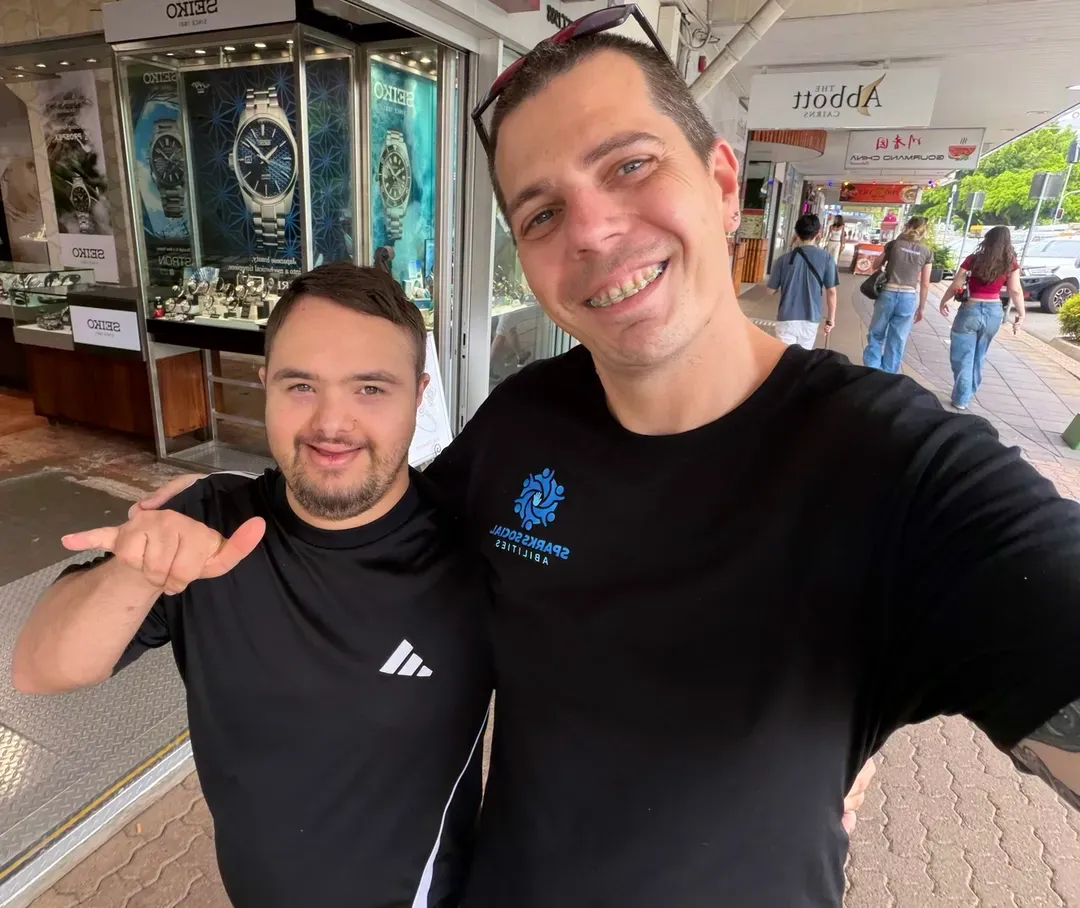 Two smiling people in black shirts taking a selfie on a covered sidewalk.