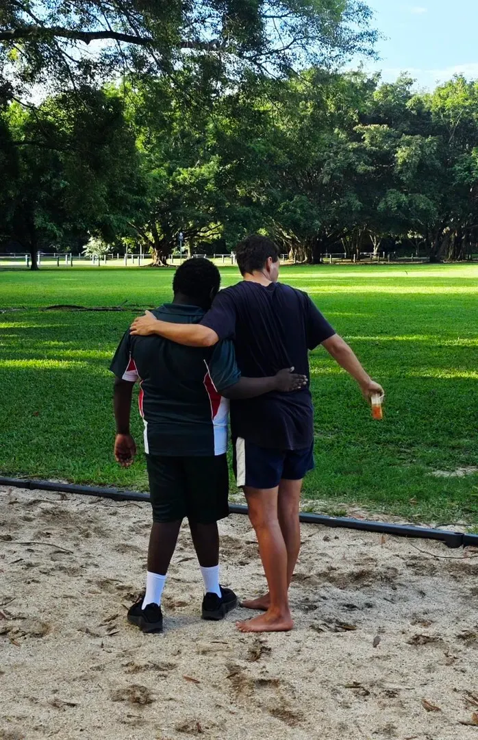Two people walking arm-in-arm on a sandy path beside a green park lawn