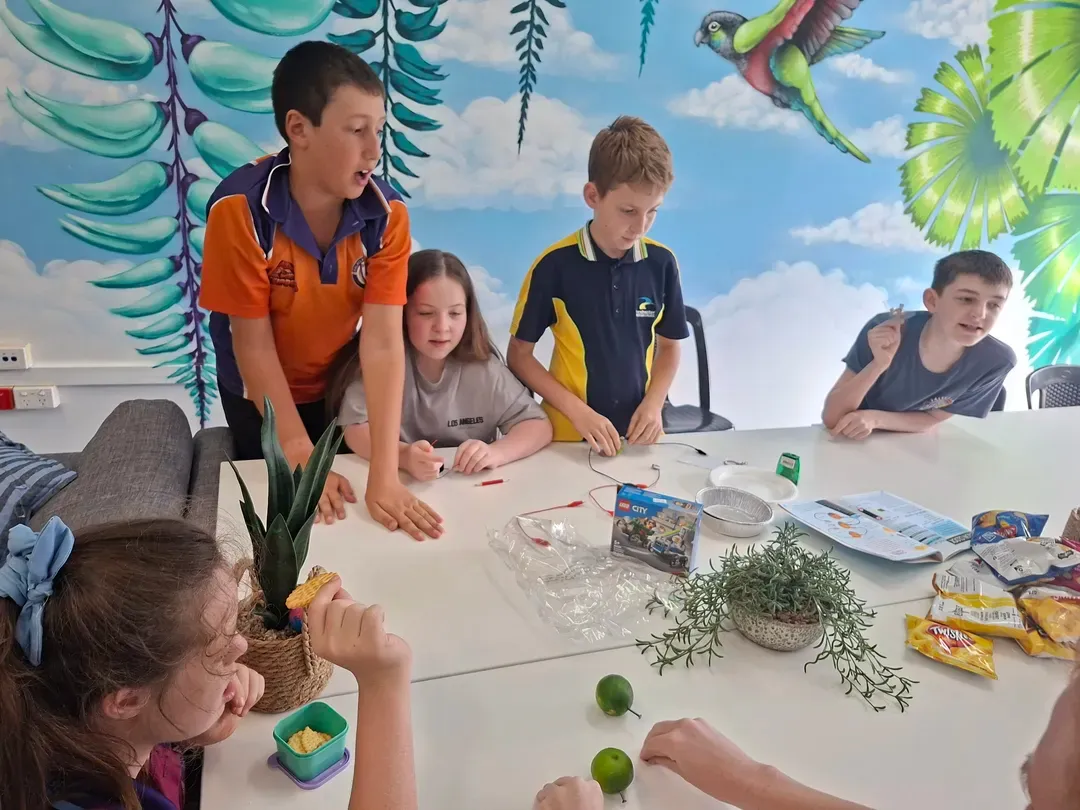 Children painting at a table in a bright classroom with a colourful mural background