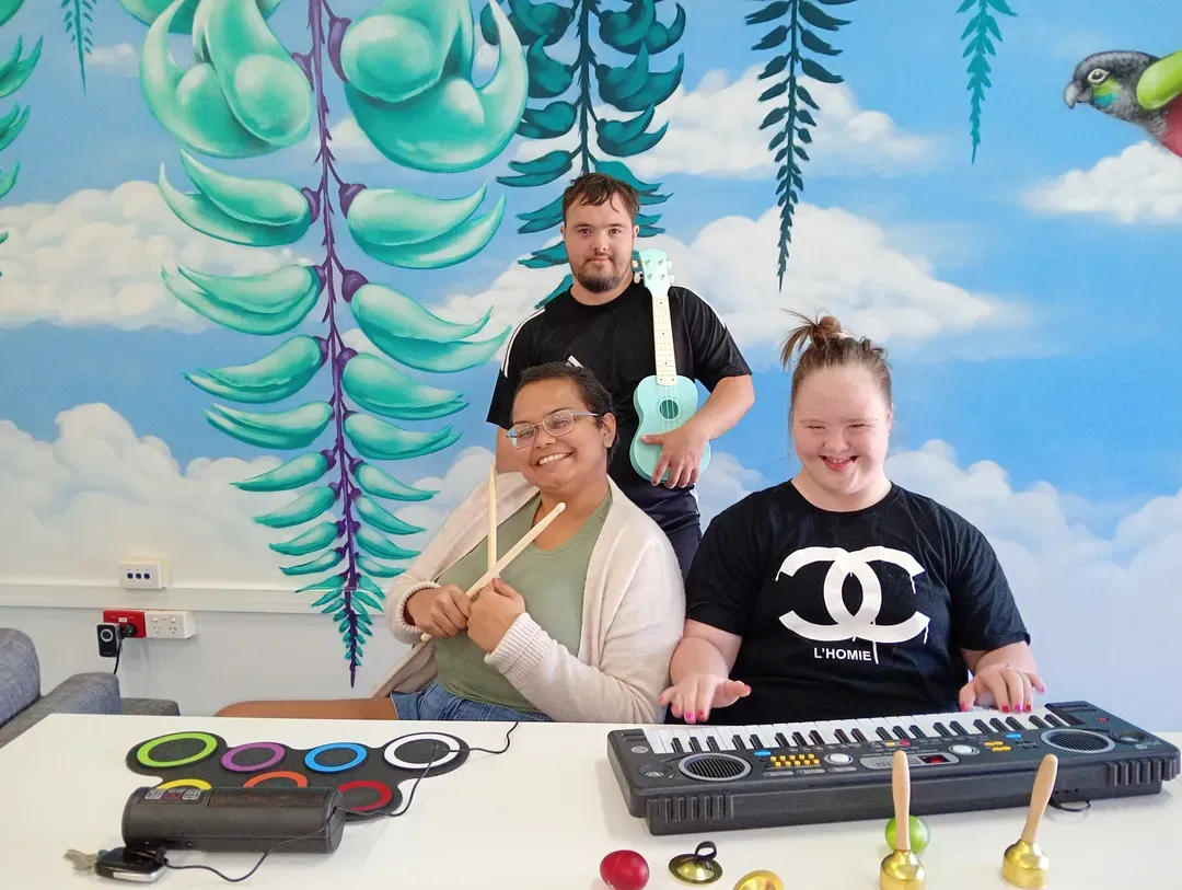 Three people making music with keyboards and drum pads in front of a blue mural.