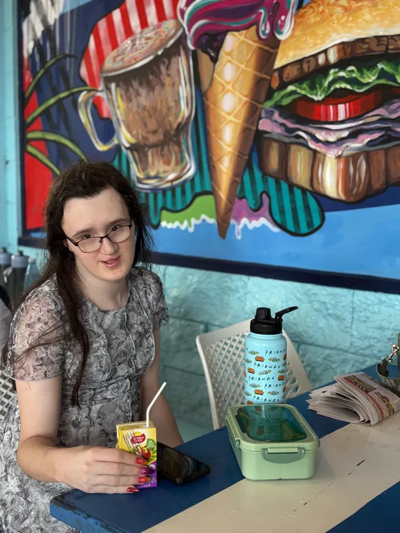 Person seated at a café table with a mural of ice cream and desserts behind them