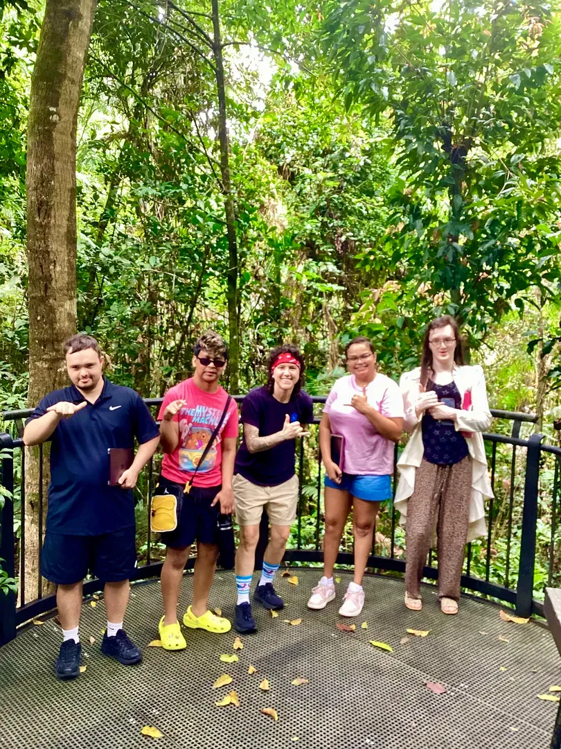 Five people posing on a forest overlook walkway, surrounded by lush green trees.