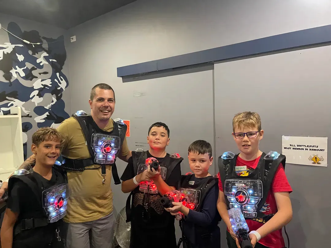 Group posing indoors, wearing black vests with glowing lights and holding props, smiling at the camera