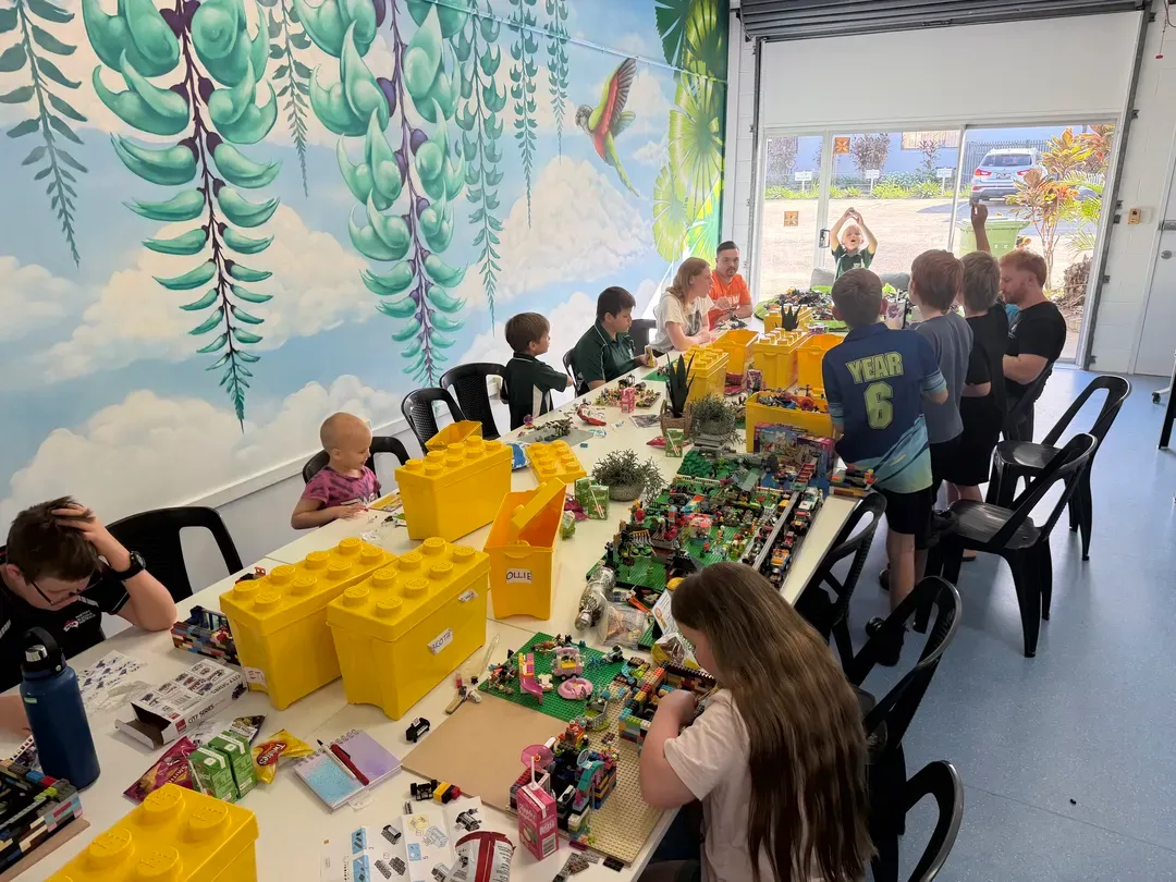 Children at a long craft table sorting colourful LEGO pieces in a bright classroom with wall mural.