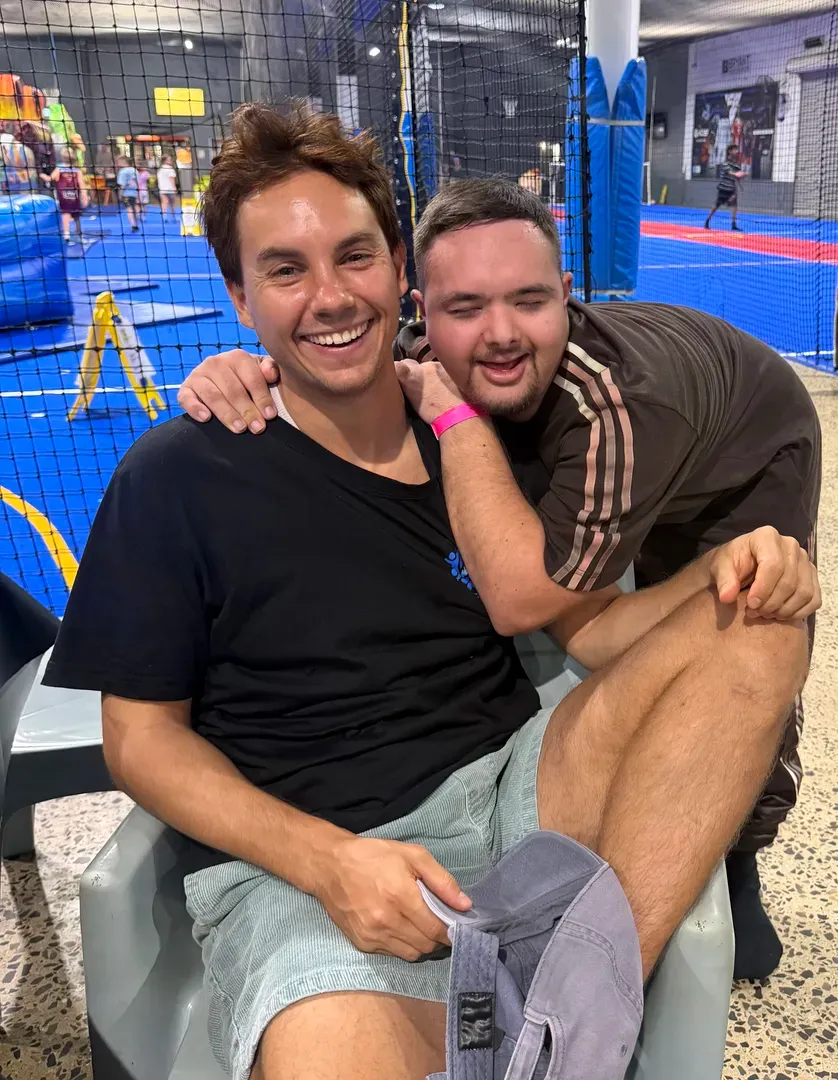 Two smiling people sitting together on a couch at an indoor play area with blue padding and nets.