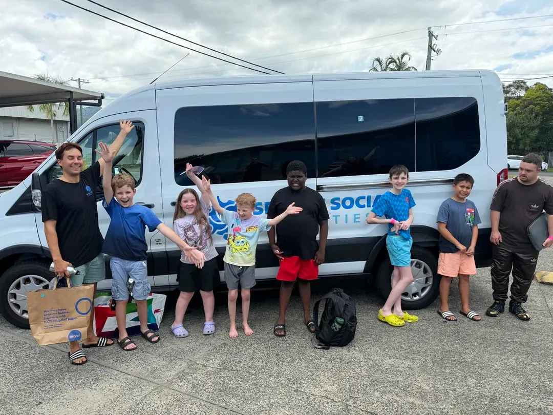 Group of volunteers standing beside a white van, holding a banner and signs on a street.
