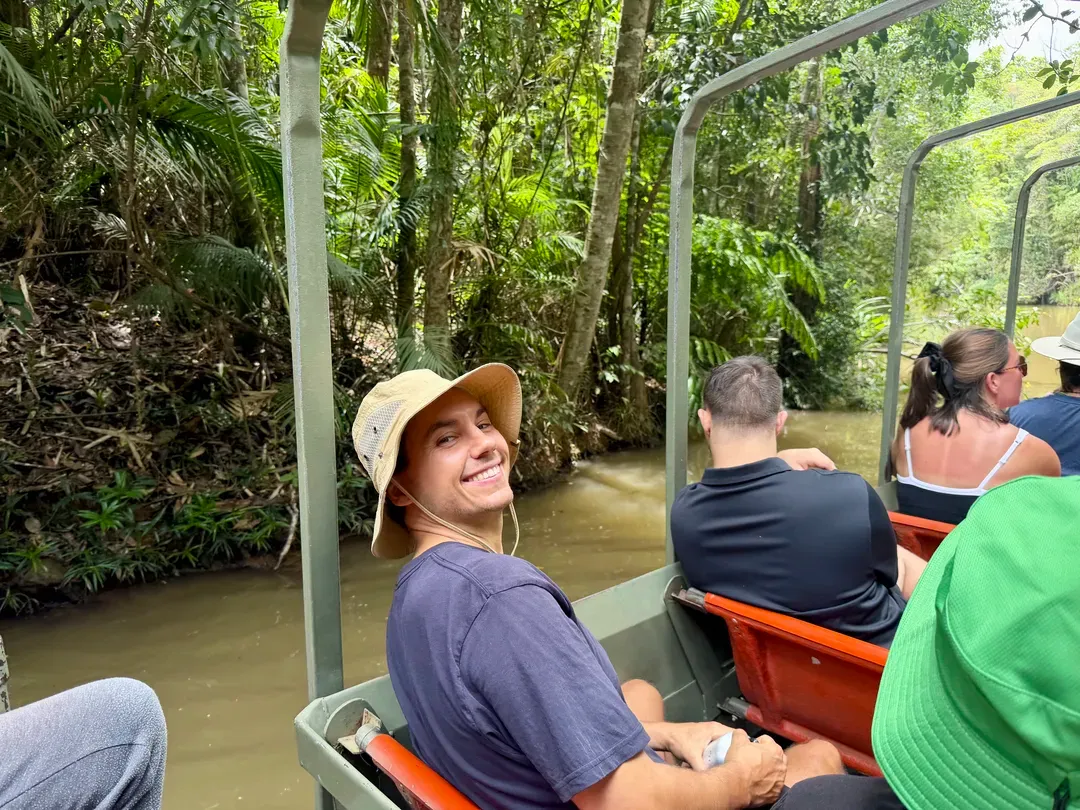 People riding an open boat through a lush green river, one smiling back at the camera.