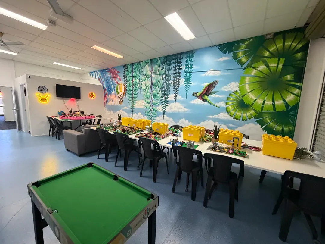 Bright indoor lounge with pool table, tables, chairs, and colourful jungle mural on the wall
