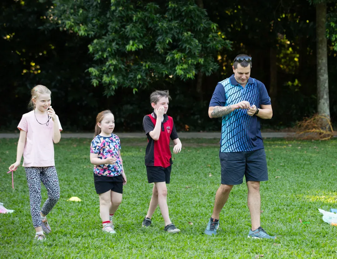 Four people walking across a grassy park, one looking at a phone