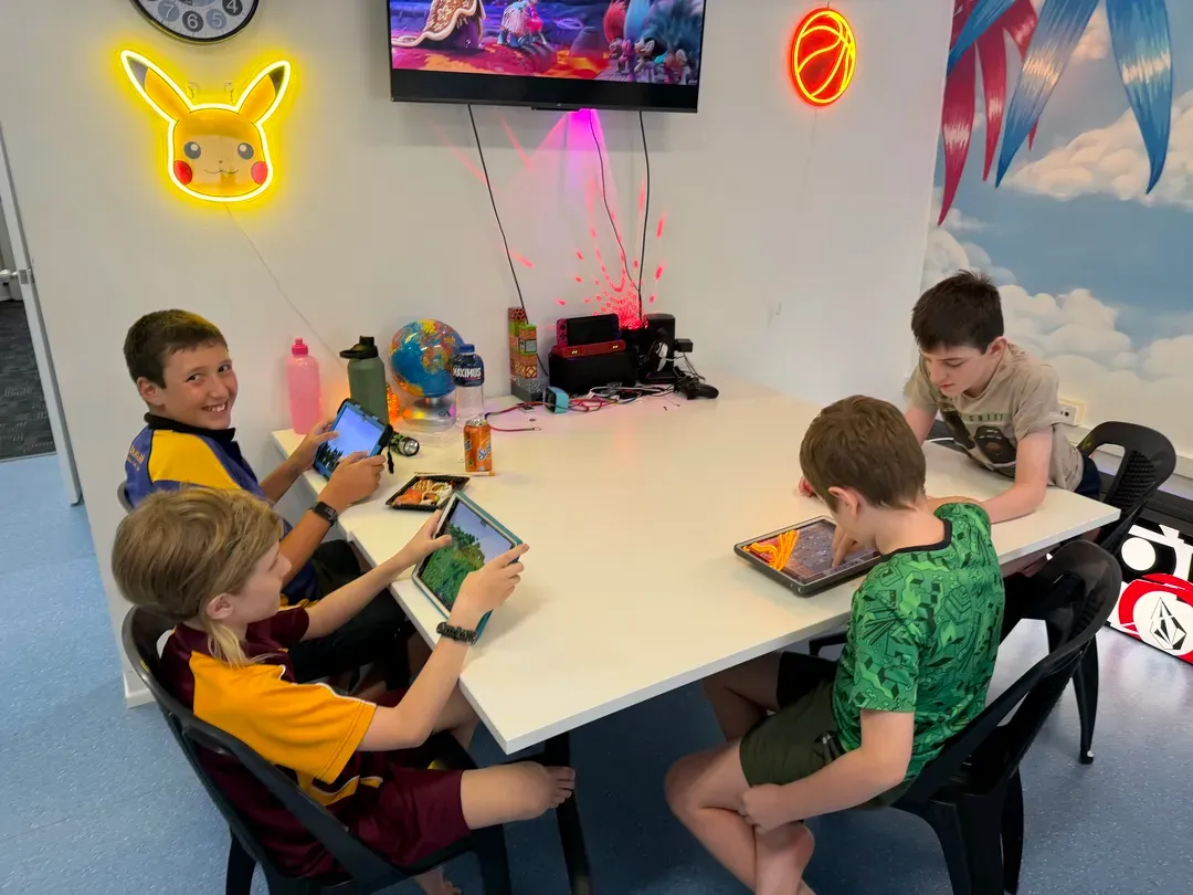 Children using tablets around a white table in a colourful playroom with neon wall lights