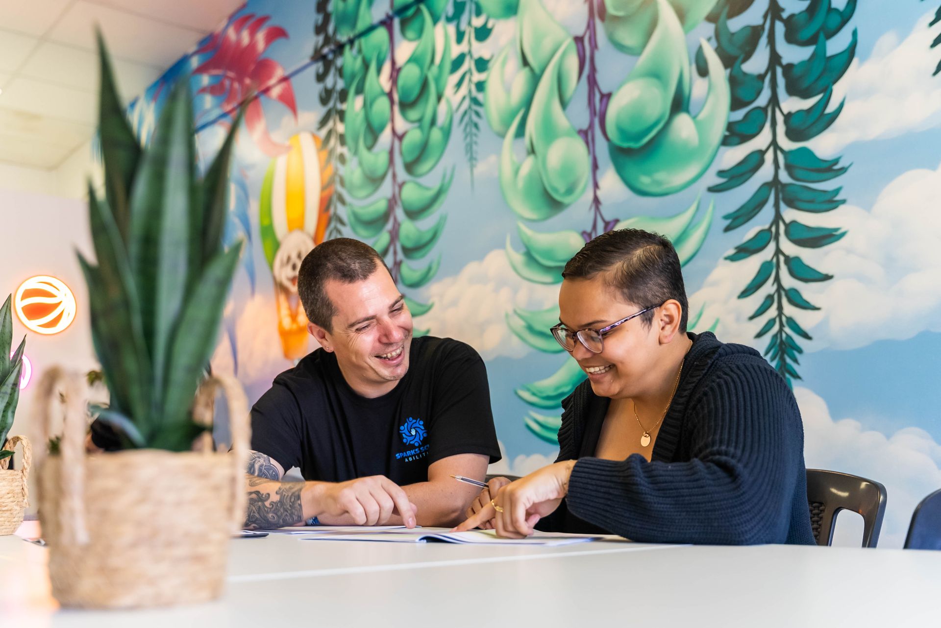 Two People Talking and Smiling Over Papers at a Table — Sparks Social Abilities in Bungalow, QLD