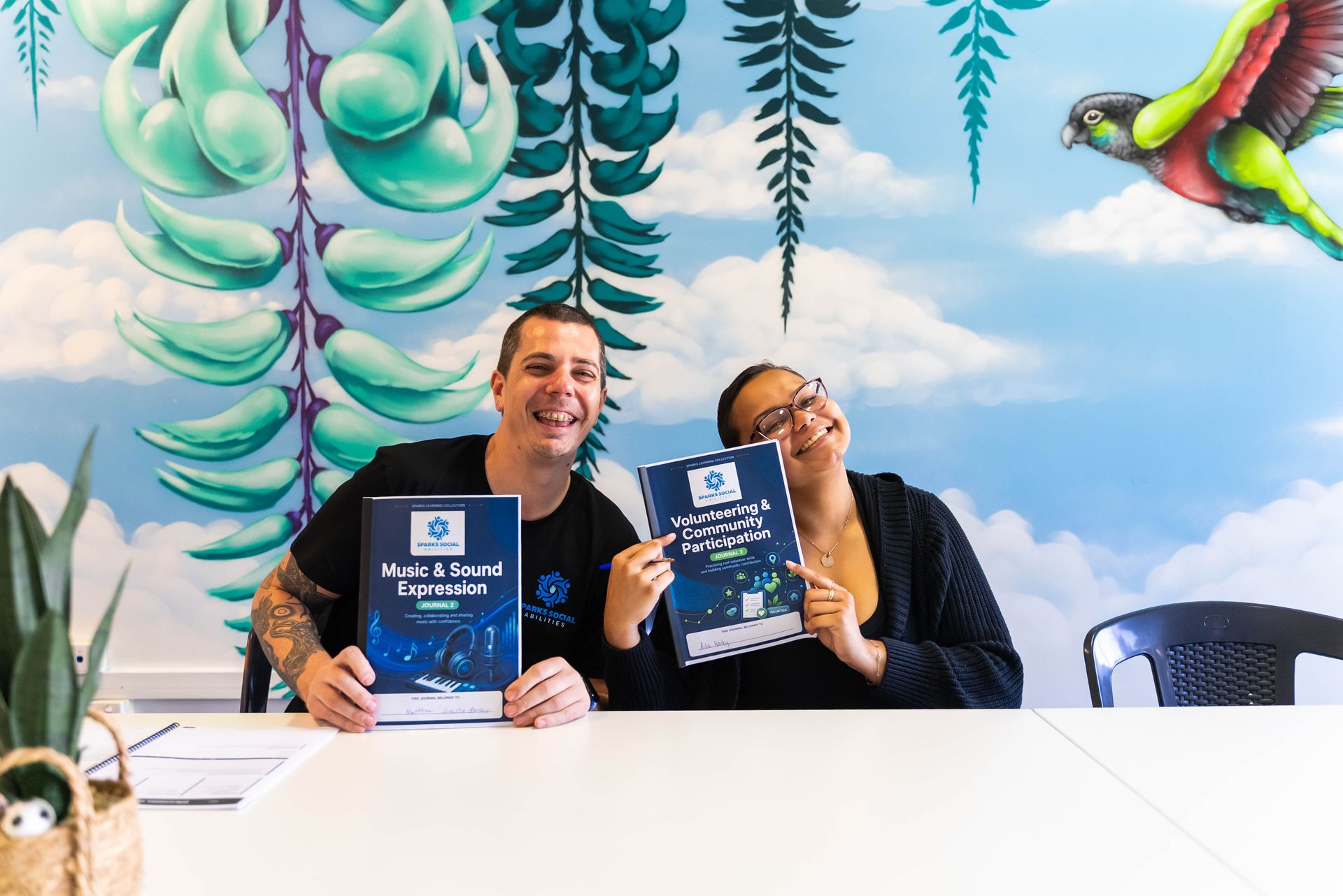 Two People Smiling and Holding Books at a White Table — Sparks Social Abilities in Bungalow, QLD