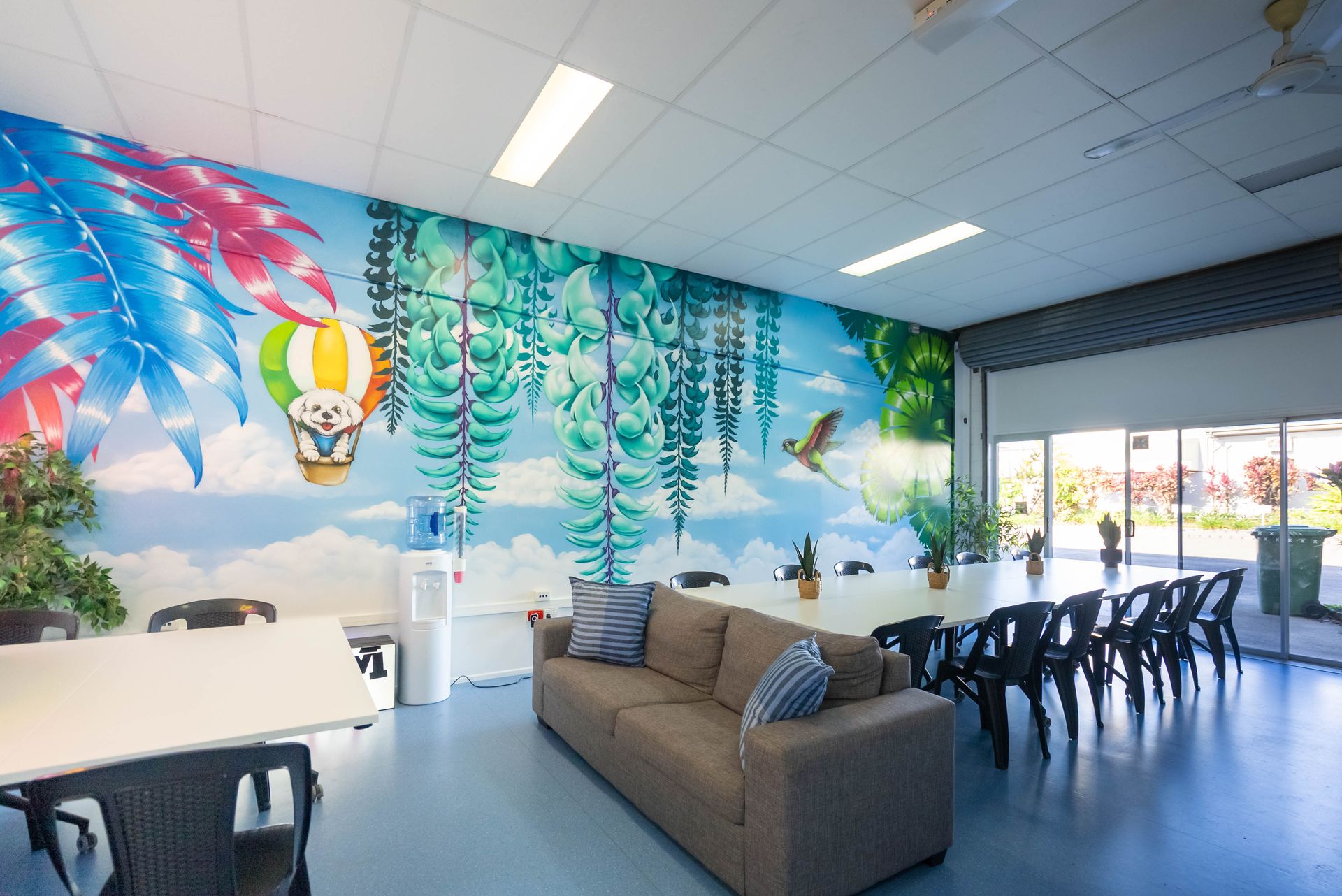 Colorful Indoor Lounge With Mural Walls, a Brown Sofa, Tables, and Stacked Chairs — Sparks Social Abilities in Bungalow, QLD