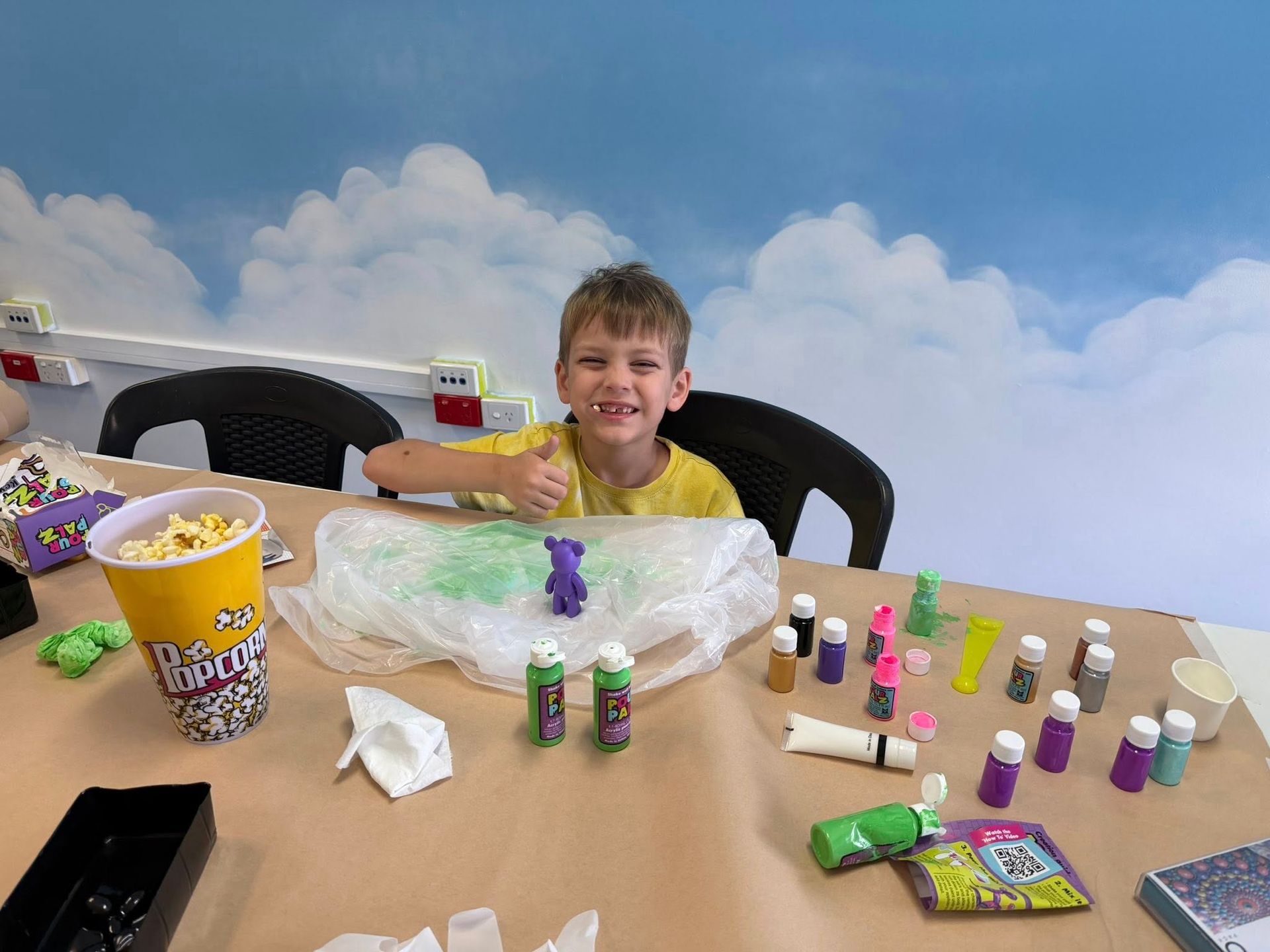 Child Smiling at a Craft Table With Small Toy Figures and Snacks — Sparks Social Abilities in Bungalow, QLD