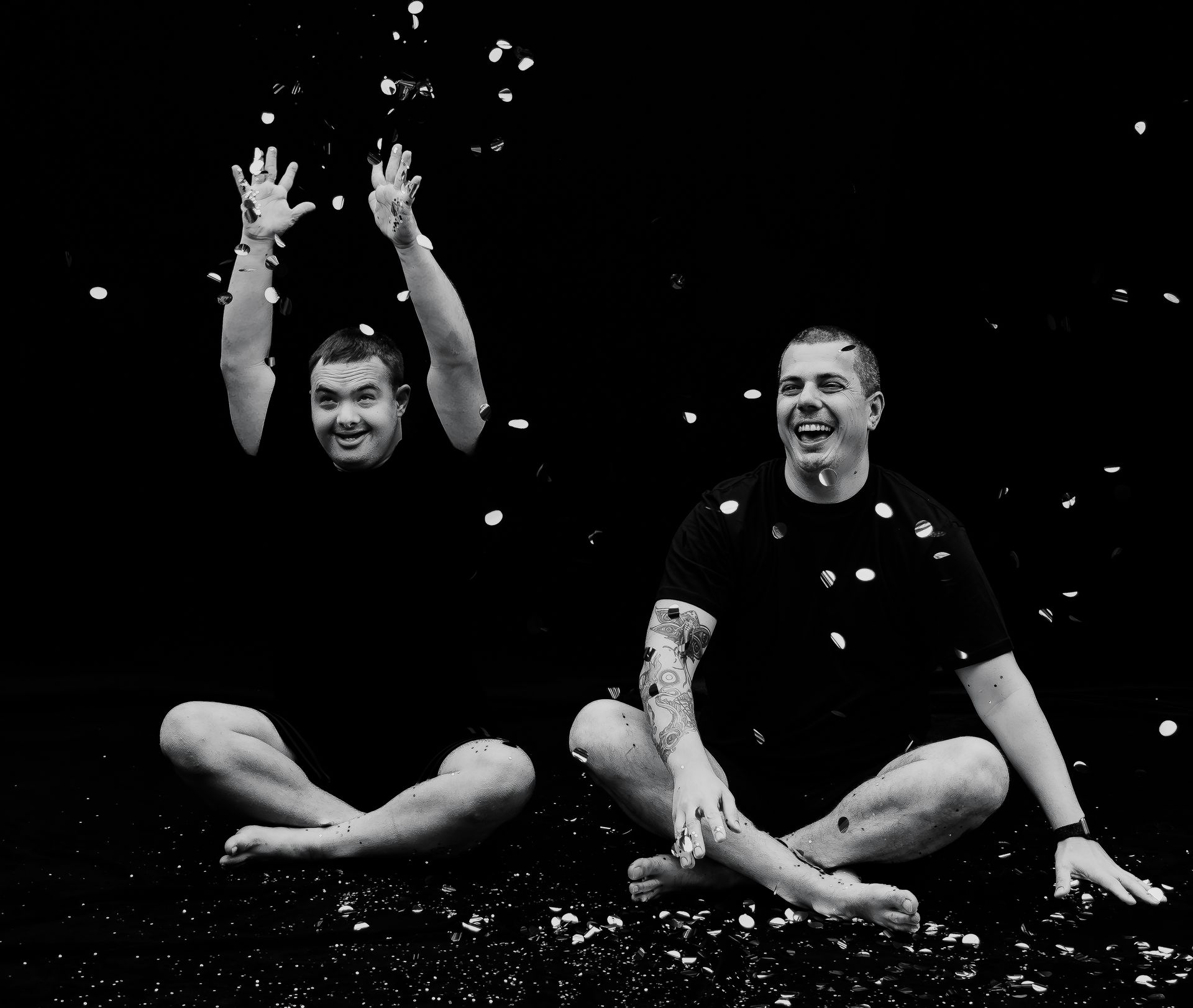 Two people sitting cross-legged in falling confetti, smiling and raising their arms on a dark stage. — Sparks Social Abilities in Bungalow, QLD