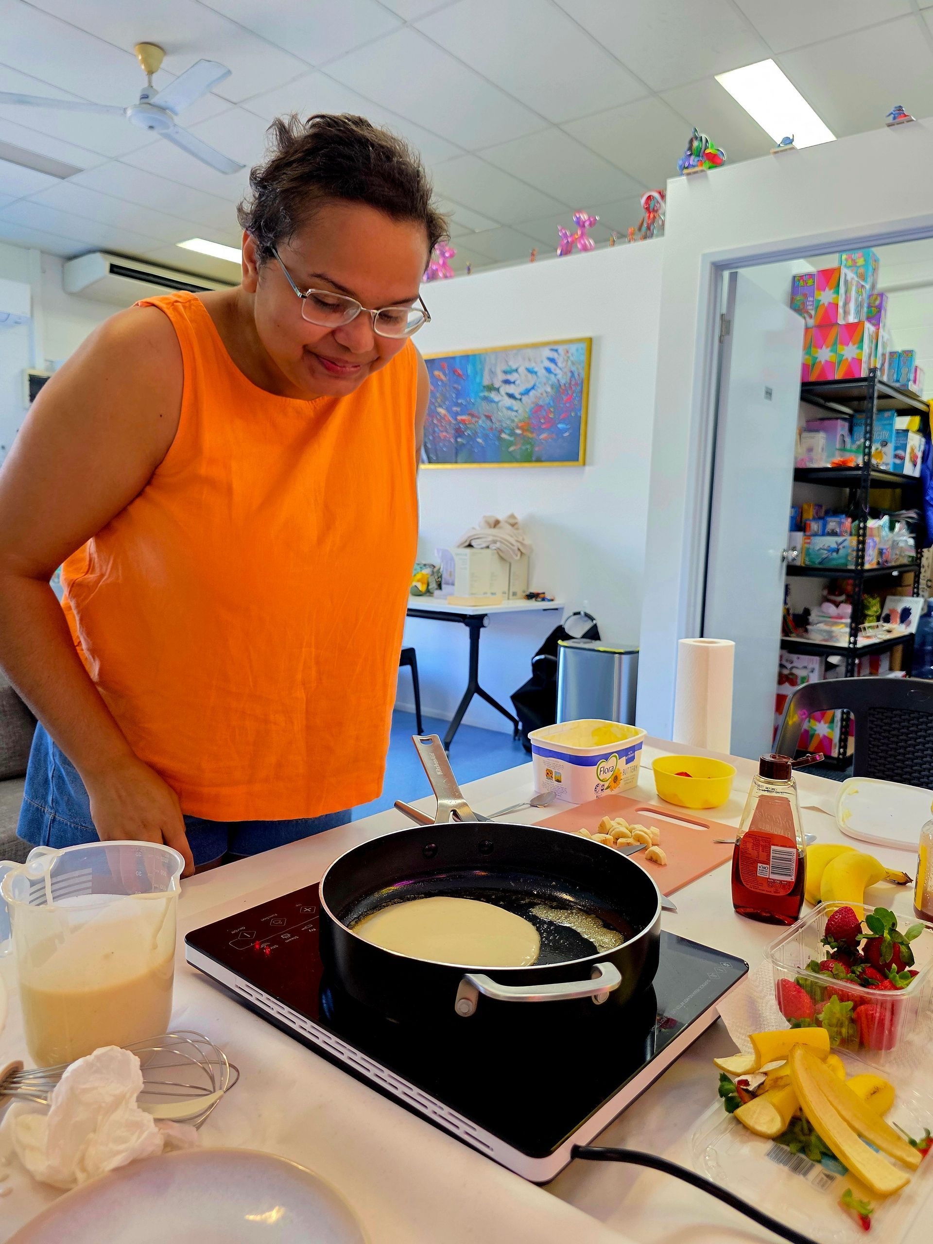 Person in an orange shirt cooking at a stovetop with ingredients laid out on the counter.