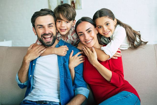 Smiling family of four sitting together on a couch, with two children hugging their parents.