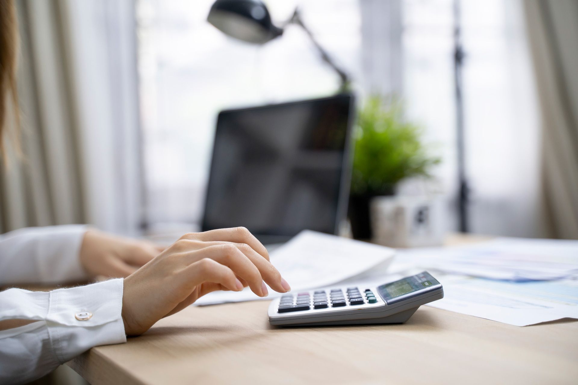 A woman is typing on a laptop while using a calculator.